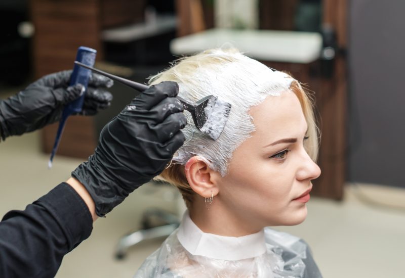 Close up of hands in black gloves are applying white color to woman hair. Hair coloring in white color at beauty salon. People and beauty concept.