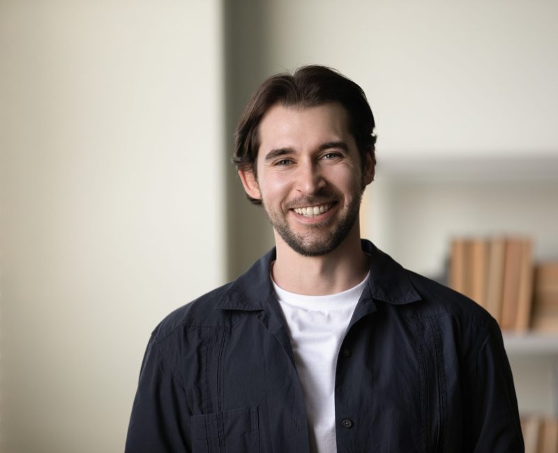 Positive successful millennial business professional man head shot portrait. Happy handsome confident young startup leader, company founder, posing in office, looking at camera with toothy smile