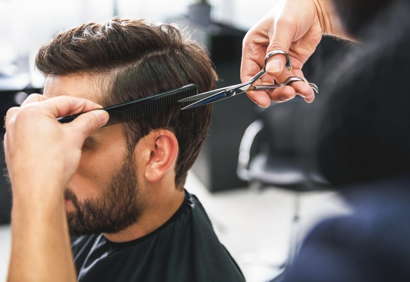 Close up of hairdresser arms cutting and combing male hair